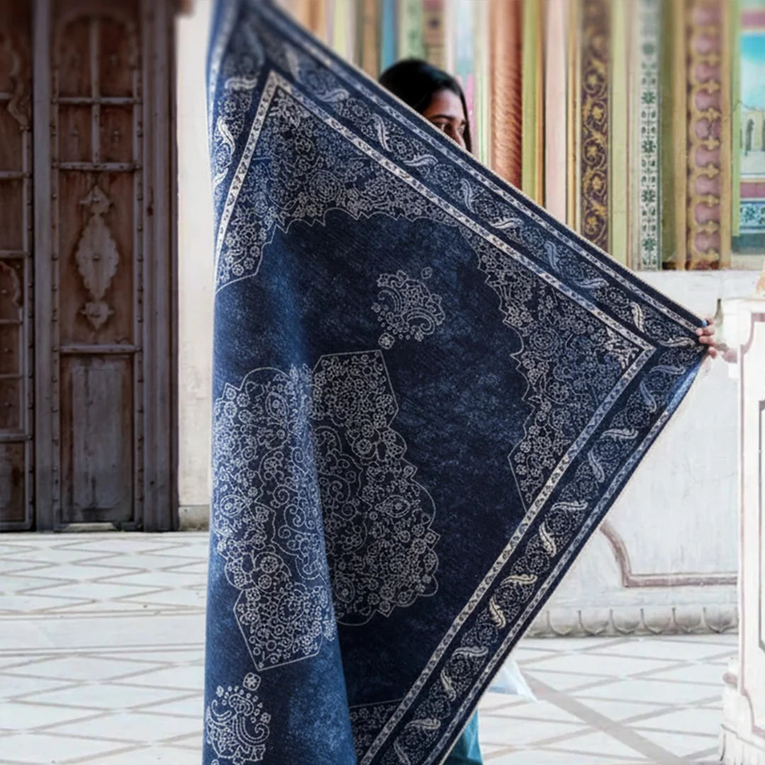 Person holding a large blue and white patterned rug indoors.